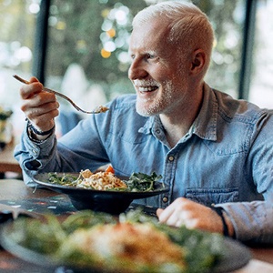 Senior man in denim shirt smiling while eating at restaurant
