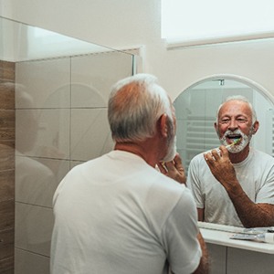 Senior man smiling while brushing teeth in bathroom
