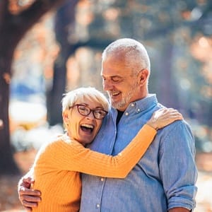 An older couple outside laughing and smiling because of the new confidence they have in their smiles