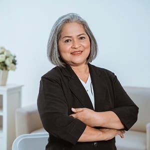 An older woman wearing a black blazer with her arms folded and smiling because of her new and improved smile