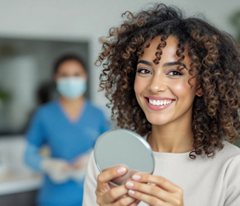 Woman smiling while holding small mirror in treatment chair