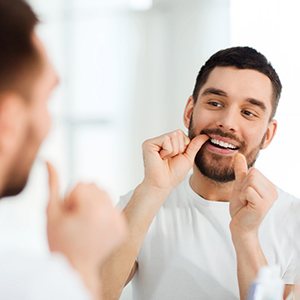 Man in white shirt smiling while flossing his teeth