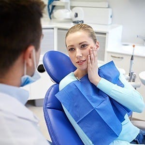 Woman in dental chair holding cheek