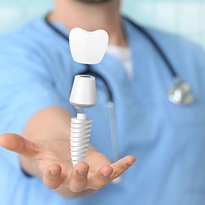 dentist smiling while holding dental implant model