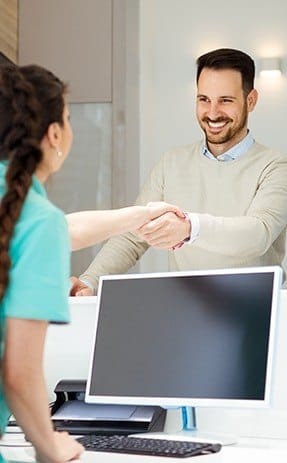 Dental team member shaking hands with dental patient at front desk