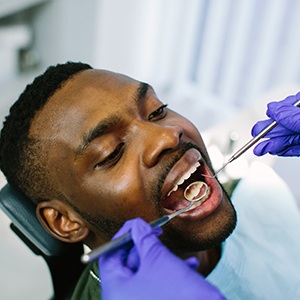 Dentist with blue gloves using dental tools to examine patient's teeth