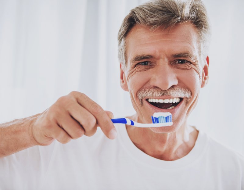 an older gentleman preparing to brush his teeth as part of his dental bridge maintenance routine