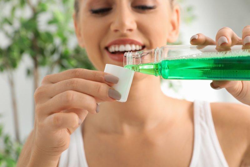 a young woman pouring herself a cap full of mouthwash