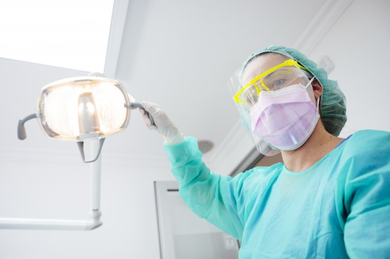 a dental staff member wearing personal protective equipment and adjusting the light for a patient