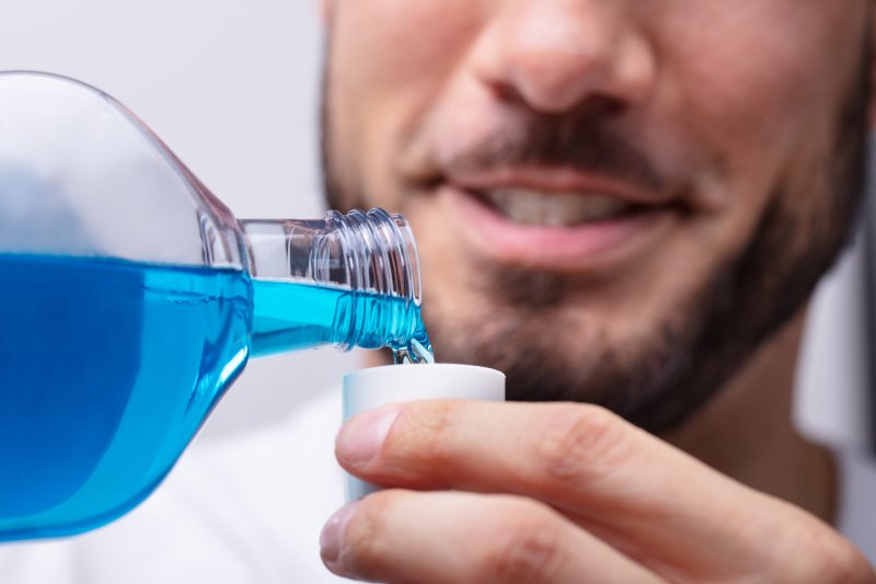 a man pouring mouthwash into a cup so he can rinse before seeing his dentist in North Naples