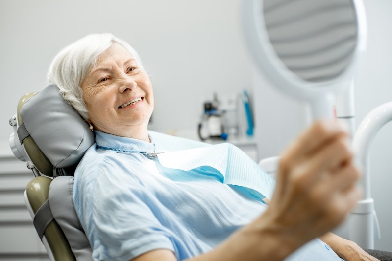 an older woman sitting in dentist’s chair pleased with her new dental implants