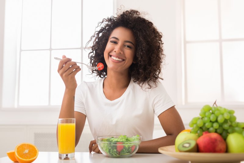 a young woman eating a salad and smiling while surrounded by various fruits and orange juice