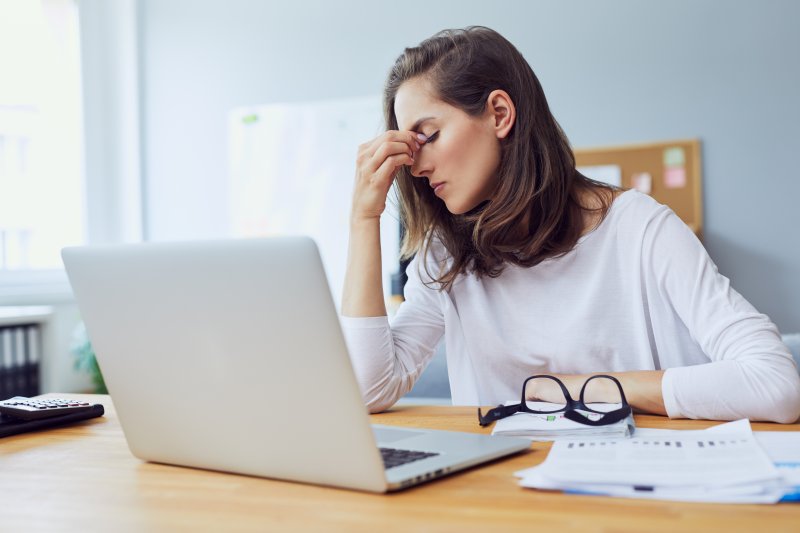 a young woman sitting behind her laptop and feeling stressed because of work 