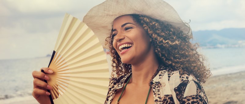a young woman standing on the beach and smiling while holding a hand fan