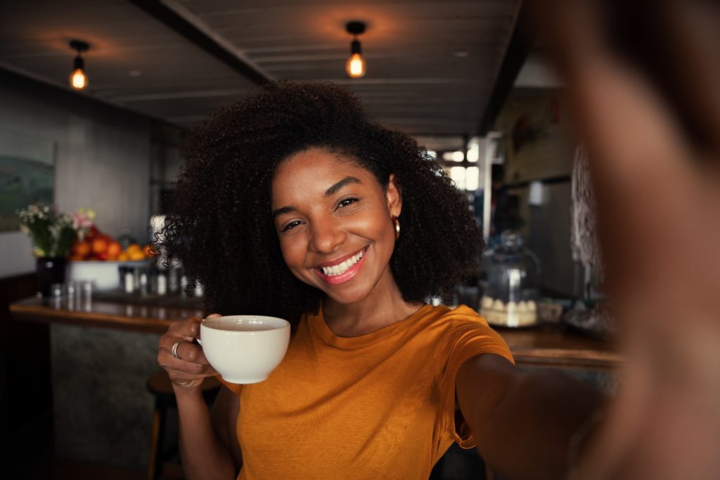 Woman in orange shirt smiling with coffee in hand