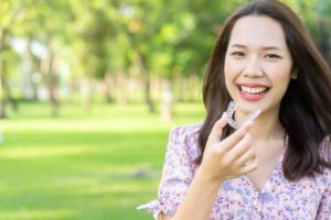 Woman standing outside in sun, holding Invisalign aligner