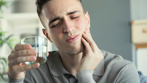 Man holding glass of water and rubbing jaw due to sensitive tooth